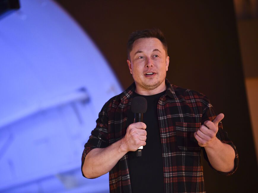 Elon Musk steht mit Mikrofon in der Hand auf der Bühne