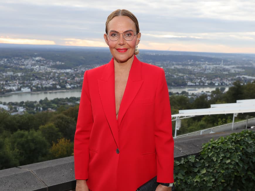 Natascha Ochsenknecht steht in einem roten Blazer oberhalb eines Flusses