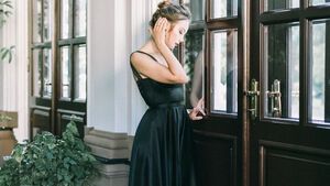 Frau mit Dutt steht im schwarzen Kleid vor Tür
