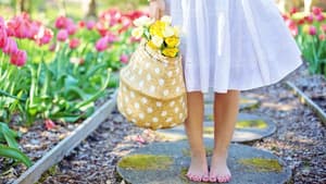Frau steht barfuß im Blumenbeet 
