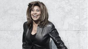 Tina Turner steht lachend vor einer grauen Wand