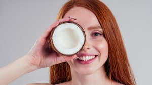 Frau hält sich eine halbe Kokosnuss vor das Gesicht