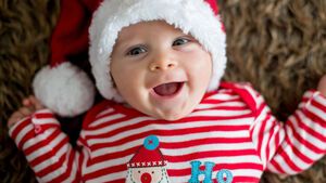 Lachendes Baby mit Weihnachtspullove rund Nikolausmütze