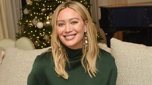 Hilary Duff sitzt lächelnd auf der Couch, im Hintergrund steht ein Weihnachtsbaum