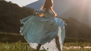 Frau tanzt in einem Kleid über eine Wiese mit Bergen im Hintergrund