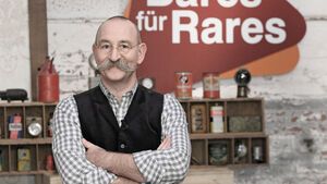  Horst Lichter mit verschränkten Armen vor dem "Bares für Rares"-Logo
