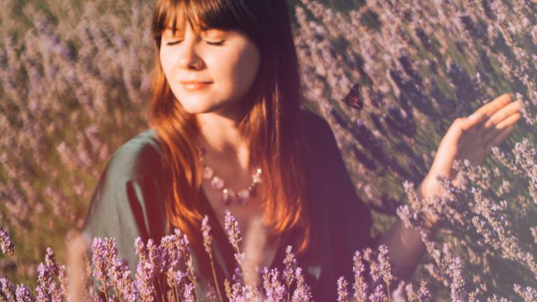 Frau mit geschlossenen Augen lächelt entspannt auf dem Lavendelfeld