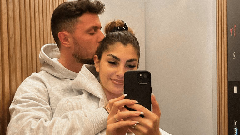 Yeliz Koc wird von hinten von Jannik Kontalis umarmt und bekommt einen Kuss auf die Wange während sie ein Selfie im Spiegel macht
