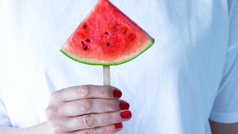 Rot lackierte Hand hält eine Wassermelone vor ein weißes Shirt
