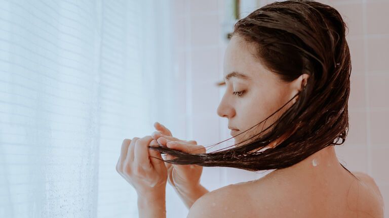 Frau mit Haarkur unter der Dusche