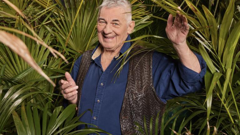 Heinz Hoenig lacht und winkt im Porträt für das Dschungelcamp 2024 im Gebüsch