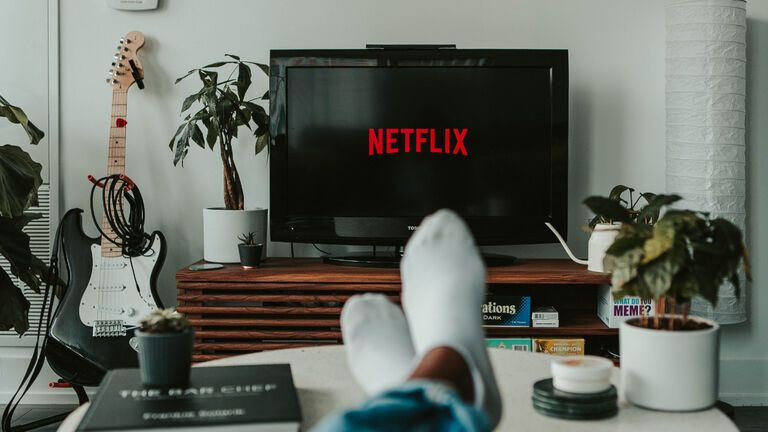 Füße liegen auf einem Couchtisch, davor steht ein Fernseher mit Netflix-Logo